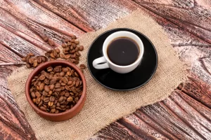 Coffee cup with roasted coffee beans on rustic wooden table.