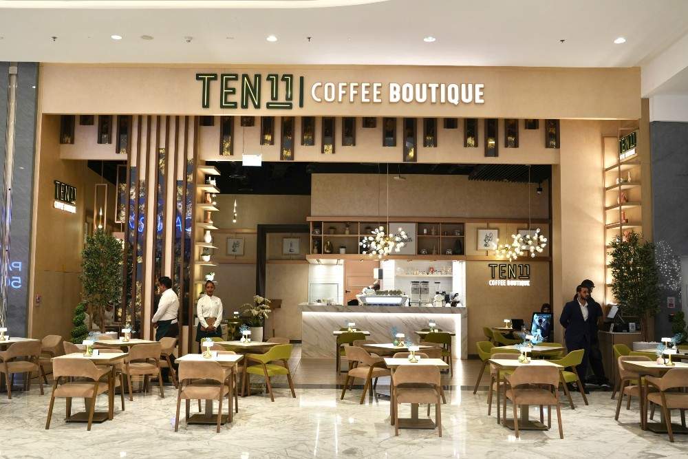 Front view of TEN11 Coffee Boutique featuring elegant modern interiors, warm lighting, beige and green seating, marble flooring, and a luxury café ambiance inside a shopping mall in the UAE.